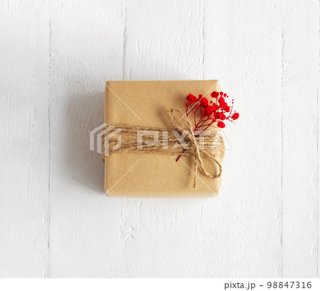 Gift box of craft paper with red flowers on the white wooden background. Valentine's Day. Happy birthday. Gift box of craft paper with red flowers on the white wooden background. Valentine's Day. Happy birthday. 98847316