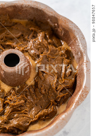 Filling metal bundt cake pan with cake butter to bake gingerbread bundt cake with caramel filling. 98847657