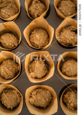 Scooping dough with dough scoop into cupcake pan lined with tulip paper muffin liners to bake banana oatmeal muffins. Scooping dough with dough scoop into cupcake pan lined with tulip paper muffin liners to bake banana oatmeal muffins. 98847686