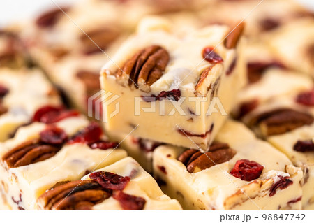 Cutting white chocolate cranberry pecan fudge into small pieces on a white cutting board. 98847742