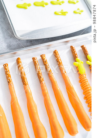 Dipped in chocolate pretzel rods on a baking sheet with parchment paper. 98847874