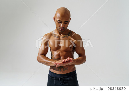 Attractive Sportsman with naked torso is warming up on white studio background Attractive Sportsman with naked torso is warming up on white studio background 98848020
