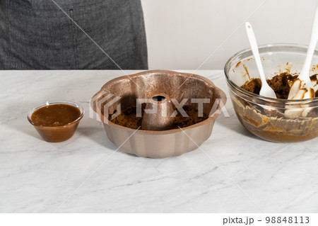 Filling metal bundt cake pan with cake butter to bake gingerbread bundt cake with caramel filling. 98848113