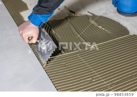 Tiler worker placing or tiling gray ceramic tile in the position over adhesive glue with lash tile leveling system, renovation or recontruction, concept of building 98853659