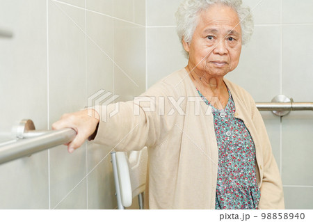 Asian elderly old woman patient use toilet support rail in bathroom, handrail safety grab bar, security in nursing hospital. 98858940