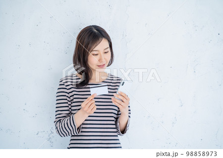 明るいリビングでスマートフォンとクレジットカードを持つ笑顔の30代女性一人 明るいリビングでスマートフォンとクレジットカードを持つ笑顔の30代女性一人 98858973