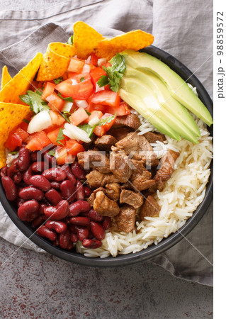 Chifrijo is a unique Costa Rican dish made by layering the following components rice, beans, chicharron pork, pico de gallo and tortilla chips closeup. Vertical top view Chifrijo is a unique Costa Rican dish made by layering the following components rice, beans, chicharron pork, pico de gallo and tortilla chips closeup. Vertical top view 98859572