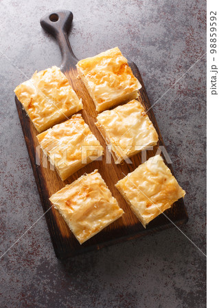 Galaktoboureko is a traditional Greek dessert featuring a custard in a crispy phyllo pastry closeup on the wooden board. Vertical top view Galaktoboureko is a traditional Greek dessert featuring a custard in a crispy phyllo pastry closeup on the wooden board. Vertical top view 98859592