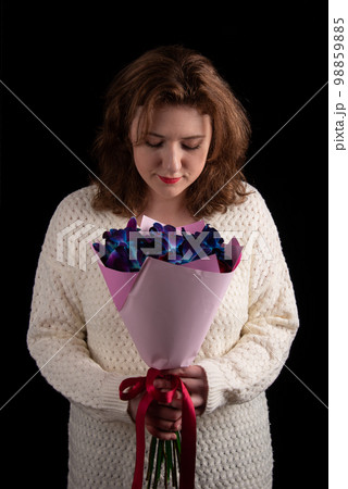 Attractive young woman smiling looking at a bouquet of orchids and roses against a black background. 98859885