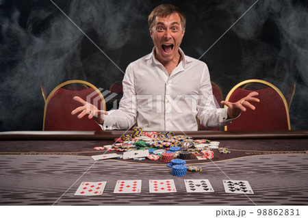 Handsome emotional man is playing poker sitting at the table in casino. 98862831