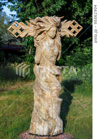 A wooden sculpture of a dancing girl stands against a blurred background of a green park. 06.19.2022. Kyiv. Ukraine. 98862904