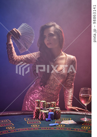 Brunette girl with a perfect hairstyle and bright make-up is posing with fan of hundred dollar bills in her hands. Casino, poker. Brunette girl with a perfect hairstyle and bright make-up is posing with fan of hundred dollar bills in her hands. Casino, poker. 98863141