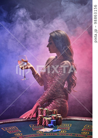 Brunette girl with a perfect hairstyle and bright make-up is posing with a glass of champagne in her hand. Casino, poker. Brunette girl with a perfect hairstyle and bright make-up is posing with a glass of champagne in her hand. Casino, poker. 98863156
