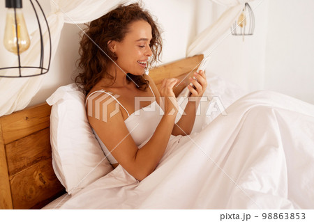 Happy Woman Holding Smartphone. Girl Using Smartphone And Smiling in Bed Happy Woman Holding Smartphone. Girl Using Smartphone And Smiling in Bed 98863853