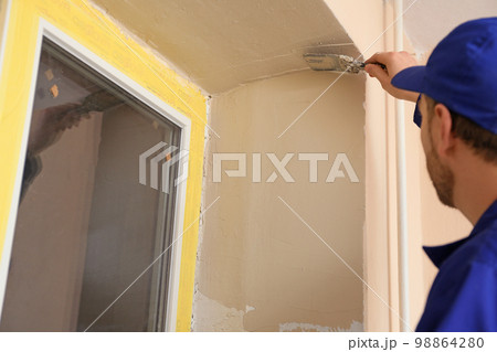 Professional worker plastering window area with putty knife indoors, closeup. Interior repair Professional worker plastering window area with putty knife indoors, closeup. Interior repair 98864280