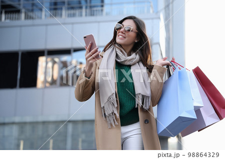 Beautiful young woman with shopping bags and smartphone outdoors 98864329