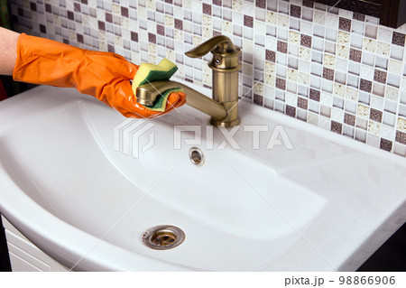 Maid is cleaning brass faucet in bathroom to remove limescale. 98866906