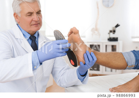 Male orthopedist fitting insole on patient's foot in clinic 98866993