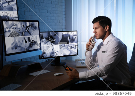 Male security guard talking by telephone near monitors at workplace Male security guard talking by telephone near monitors at workplace 98867049