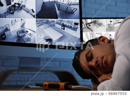 Male security guard sleeping near monitors at workplace Male security guard sleeping near monitors at workplace 98867050