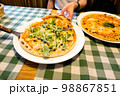 Female hands taking slices of authentic Italian caesar stone oven pizza with arugula, sauce, grilled chicken, herbs and spicy parmesan cheese. 98867851