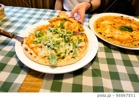 Female hands taking slices of authentic Italian caesar stone oven pizza with arugula, sauce, grilled chicken, herbs and spicy parmesan cheese. Female hands taking slices of authentic Italian caesar stone oven pizza with arugula, sauce, grilled chicken, herbs and spicy parmesan cheese. 98867851