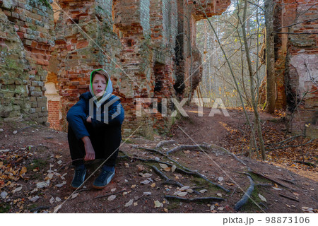 A teenager sits in an old abandoned house. 98873106
