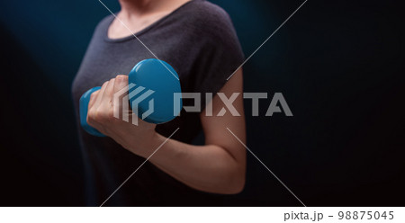 Exercising, Workout with Dumbbell. Sport and Recreation Concept. Close-up of Woman with blue Dumbbell in Dark Room at Home or Gym 98875045