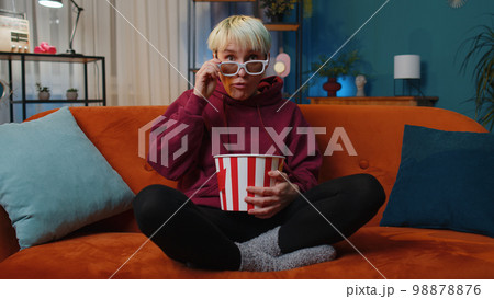 Woman sitting on couch eating popcorn and watching interesting TV serial, sport game online at home Woman sitting on couch eating popcorn and watching interesting TV serial, sport game online at home 98878876