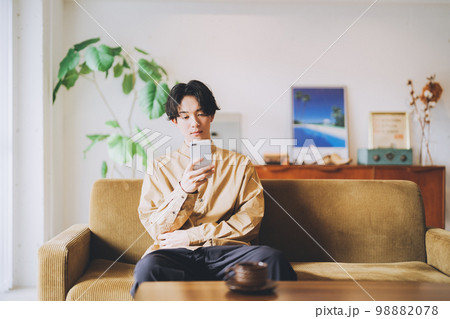 ソファに座ってスマホを見る男性 98882078