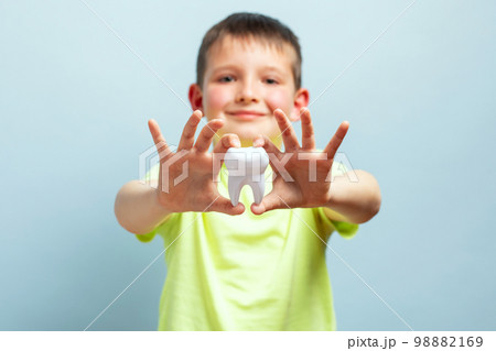 Child shows big white toy tooth on a blue background. Caring for teeth Child shows big white toy tooth on a blue background. Caring for teeth 98882169