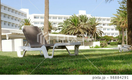 Comfortable deck chair for an ideal rest and sunbathing in a lounge zone of a hotel with green grass and palms. Mediterranean sea, Cyprus. Ayia Napa. Comfortable deck chair for an ideal rest and sunbathing in a lounge zone of a hotel with green grass and palms. Mediterranean sea, Cyprus. Ayia Napa. 98884291