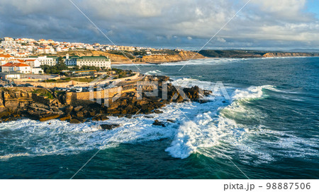Aerial view of a beautiful tourist town located on the shore of the Atlantic Ocean.  Panorama of the city from a drone with a  rocky ocean coastline during sunset. Scenic nature landscape  from drone 98887506