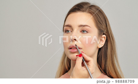 Makeup artist or stylist applies lipstick to the lips of the female model. Visagiste making make up applying lipstick on a lip. Makeup artist or stylist applies lipstick to the lips of the female model. Visagiste making make up applying lipstick on a lip. 98888709