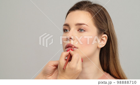 Makeup artist or stylist applies lipstick  to the lips of the female model. Visagiste making make up applying lipstick on a lip. Professional makeup. 98888710
