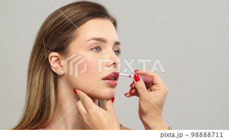 Makeup artist or stylist applies lipstick  to the lips of the female model. Visagiste making make up applying lipstick on a lip. Makeup artist or stylist applies lipstick  to the lips of the female model. Visagiste making make up applying lipstick on a lip. 98888711