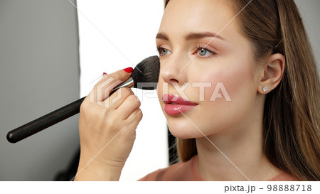 Makeup artist or stylist applies eyeshadow powder or shadows to the eyelids of the female model. Master class on applying makeup on the eyes. Beautiful woman face. Beauty fashion. Professional makeup. 98888718