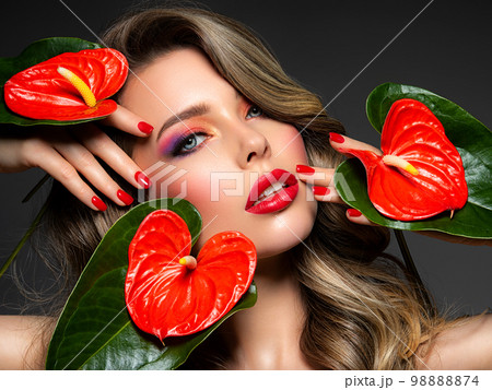 Beautiful white girl with red flowers. Stunning girl with Anthurium red. Closeup face of young beautiful blonde woman with a healthy clean skin. Pretty woman with bright makeup and long wavy hair. Beautiful white girl with red flowers. Stunning girl with Anthurium red. Closeup face of young beautiful blonde woman with a healthy clean skin. Pretty woman with bright makeup and long wavy hair. 98888874