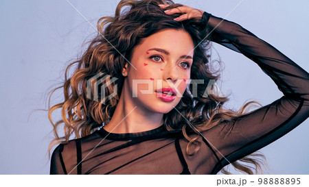Beautiful model with drawn hearts on her cheeks posing in the studio. A fashion model touching her hair is photographed in a photo studio looking away from the camera. Beautiful young woman with long Beautiful model with drawn hearts on her cheeks posing in the studio. A fashion model touching her hair is photographed in a photo studio looking away from the camera. Beautiful young woman with long 98888895