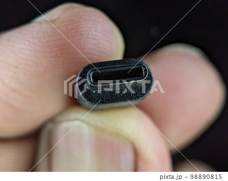 Closeup finger holding USB charger cable on a black background. 98890815