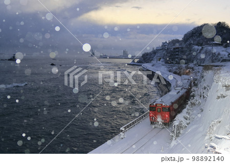 雪降る冬の氷見線（走り去る列車を後方から撮影） 98892140