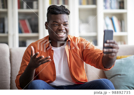 Smiling african guy have video call via phone at home Smiling african guy have video call via phone at home 98892735