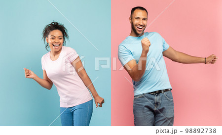 Young black guy and lady in casual having fun together, dancing over halved pink and blue studio background Young black guy and lady in casual having fun together, dancing over halved pink and blue studio background 98892738
