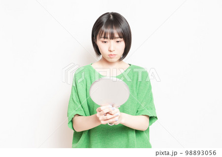 手鏡で顔を見ている若い女性 手鏡で顔を見ている若い女性 98893056
