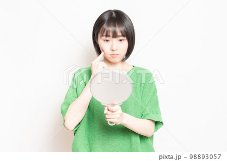 手鏡で顔を見ている若い女性 手鏡で顔を見ている若い女性 98893057