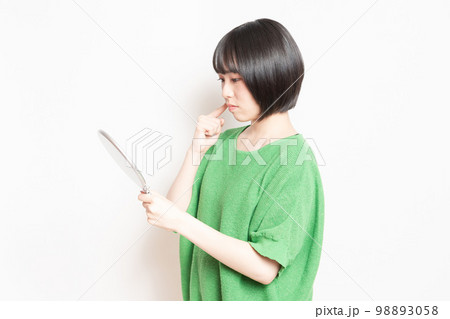 手鏡で顔を見ている若い女性 手鏡で顔を見ている若い女性 98893058