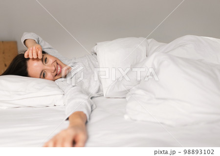 Smiling young european female sleeping on white bed, waking up, enjoying good morning, weekend Smiling young european female sleeping on white bed, waking up, enjoying good morning, weekend 98893102