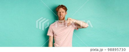 Disappointed redhead man showing thumbs-down and tongue, epxress dislike and disapproval, standing over turquoise background Disappointed redhead man showing thumbs-down and tongue, epxress dislike and disapproval, standing over turquoise background 98895730