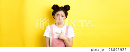 Sad and disappointed asian girl frowning, feel unfair, pointing finger right at bad thing, complaining on something upsetting, yellow background Sad and disappointed asian girl frowning, feel unfair, pointing finger right at bad thing, complaining on something upsetting, yellow background 98895925