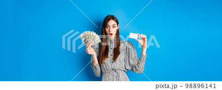 Excited lucky girl showing plastic credit card and money dollar, gasping amazed, buying something expensive, standing on blue background 98896141